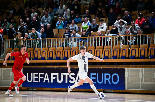 Men in red and white jerseys running after the ball in front of a packed grandstand.