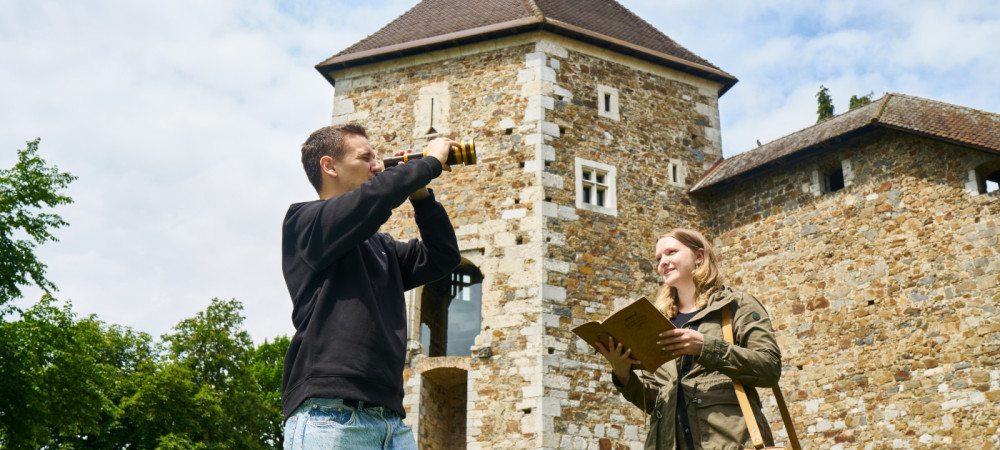 Un uomo con un binocolo e una donna con un libro in mano, con un castello sullo sfondo.