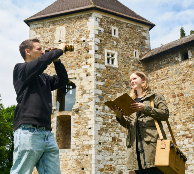 Moski z daljnogledom in zenska s knjigo v roki, v ozadju pa je grad.