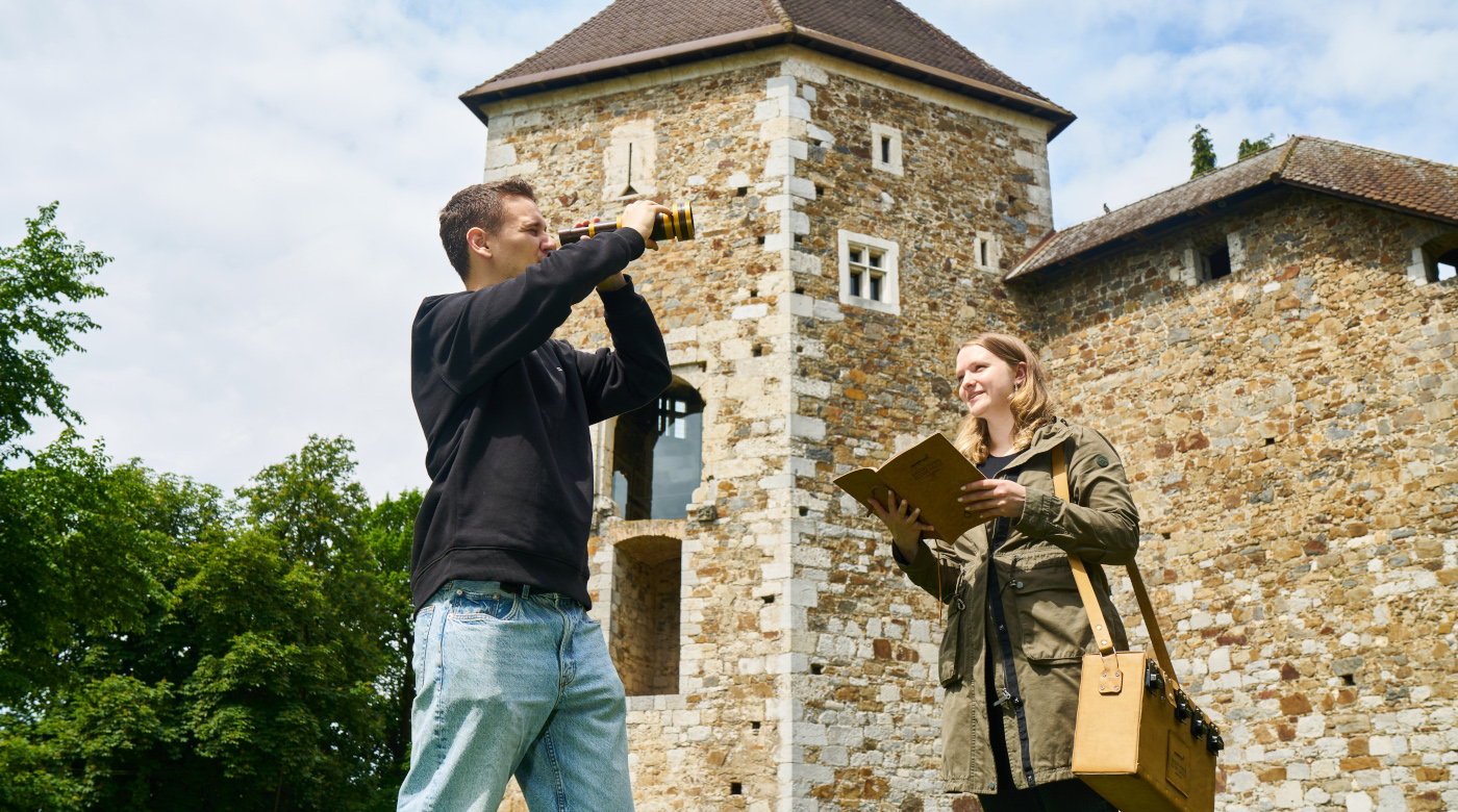 Un uomo con un binocolo e una donna con un libro in mano, con un castello sullo sfondo.