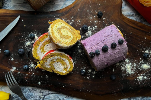 Blueberry roulade and its slices on a wooden tray.