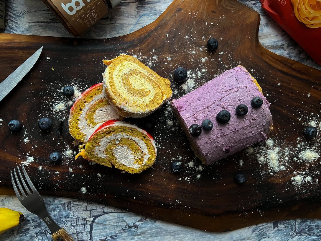 Blueberry roulade and its slices on a wooden tray.