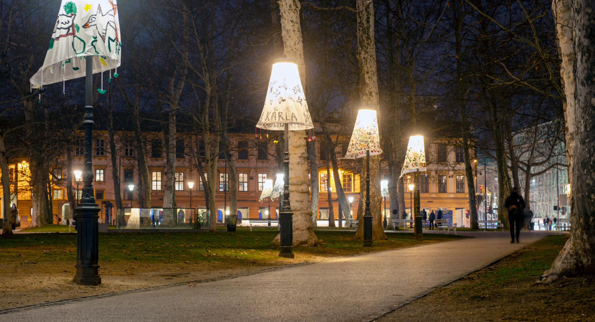 Three lamp posts with decorative shades in a park at night.