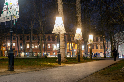 Three lamp posts with decorative shades in a park at night.