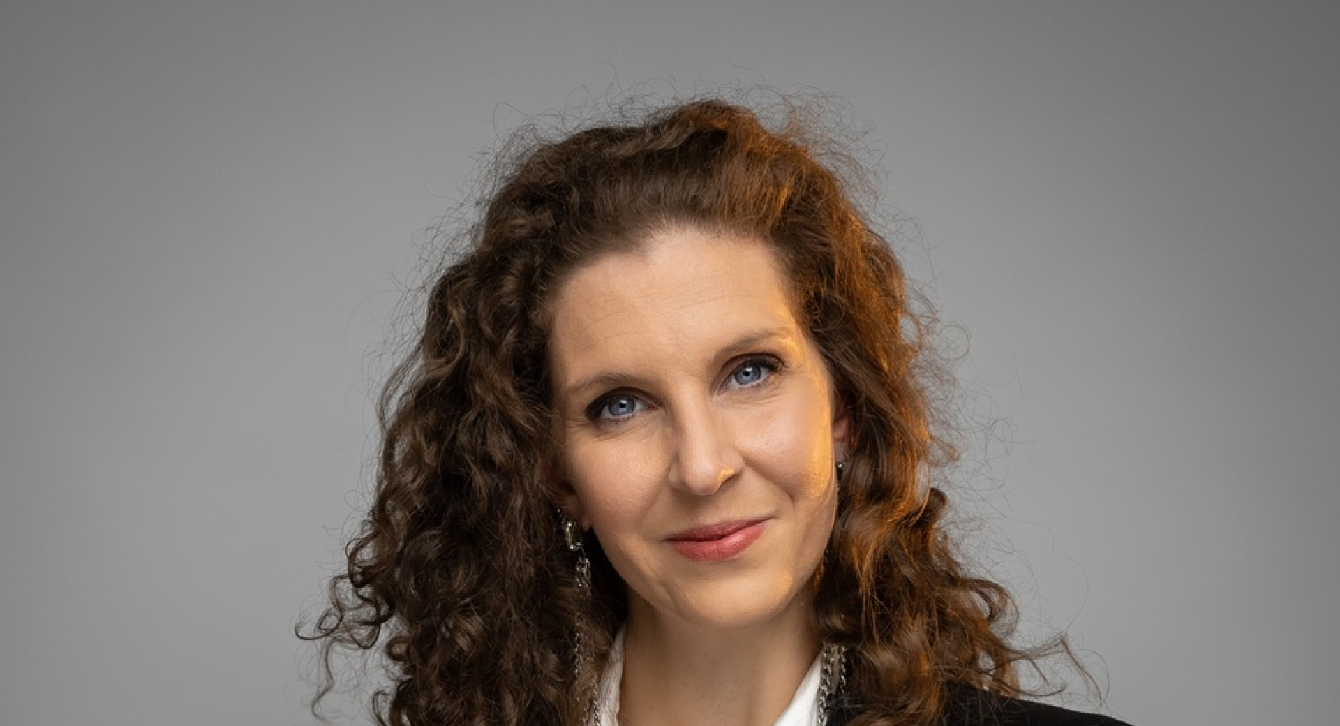 A woman with curly hair is holding five bottles of wine in her arms.