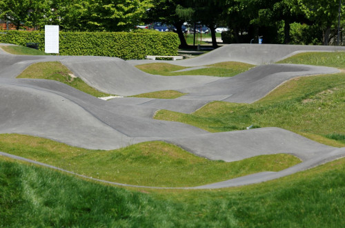 A pump track surrounded by greenery and trees features undulating asphalt paths, perfect for recreational cycling adventures.