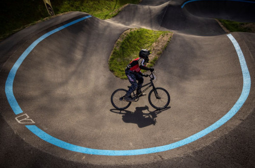 A pump track highlighted with bold blue lines, where a cyclist in protective gear is navigating a turn.
