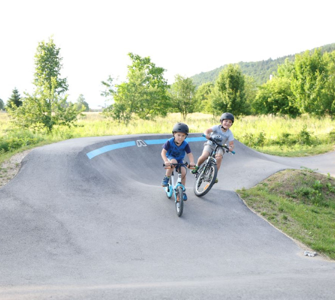 Children riding on a pumptrack surrounded by nature in the summer sun.