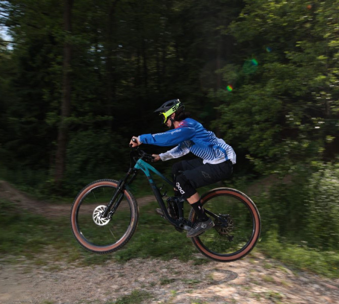A mountain biker in the air while riding through forest terrain.