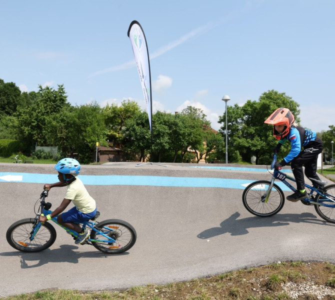 Two children cycling on a regulated polygon with helmets for safety.