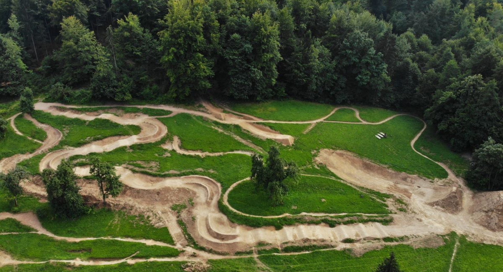 The Pumptrack polygon, set in a natural environment, consists of an undulating track with curves that stretches along the edge of the forest and offers the possibility for recreational cycling.