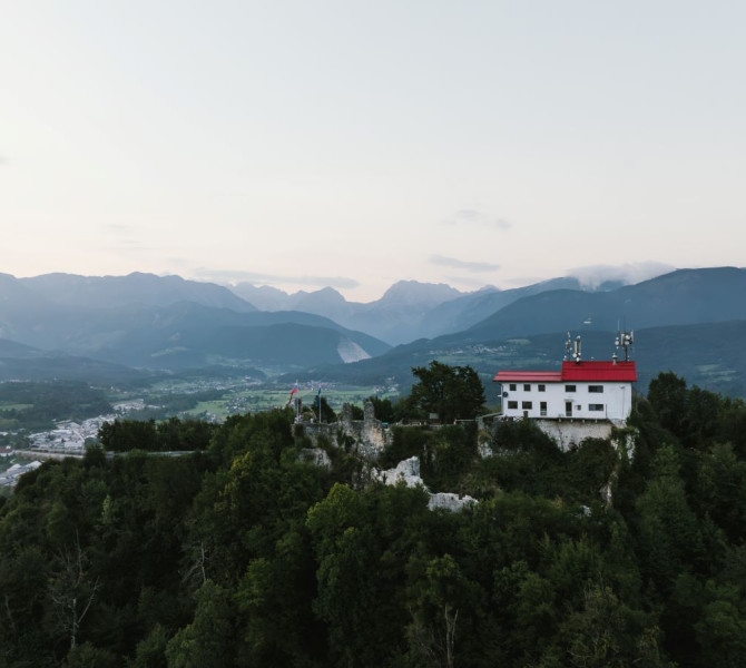 An old building with a red roof, surrounded by forests, overlooking a vast valley and mountainous landscape.