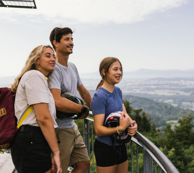 The family is enjoying the view of the surroundings from the observation tower. Family on the observation tower, they are holding cycling helmets in their hands.