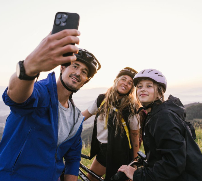 A family of three is taking a selfie with a hill and a church on top in the background.