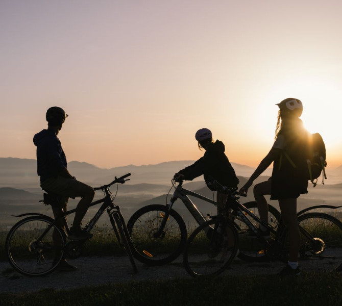Silhouettes of a family watching the sunset on their bikes in the middle of the mountains.