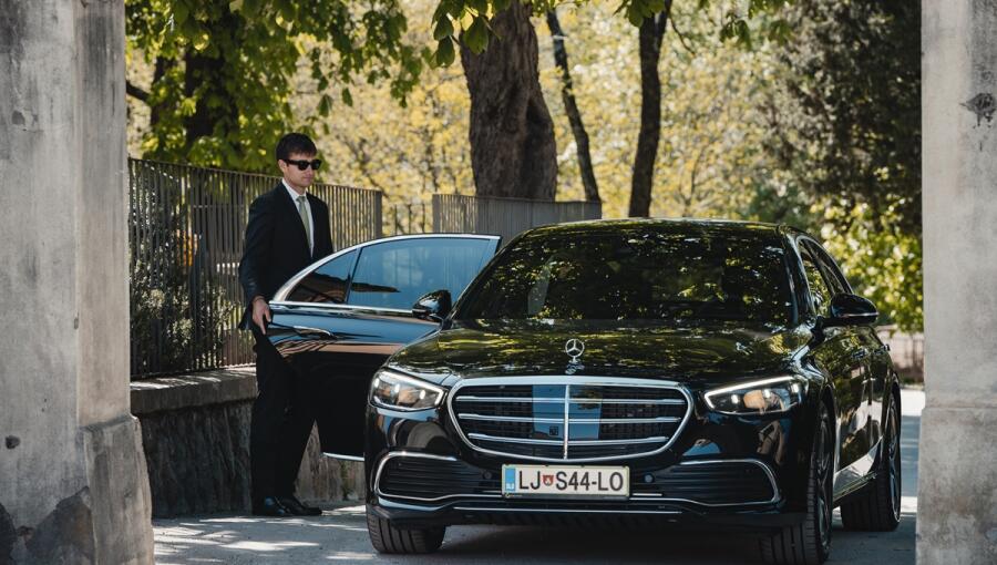 An elegant black car with a driver in a black suit opening the door.
