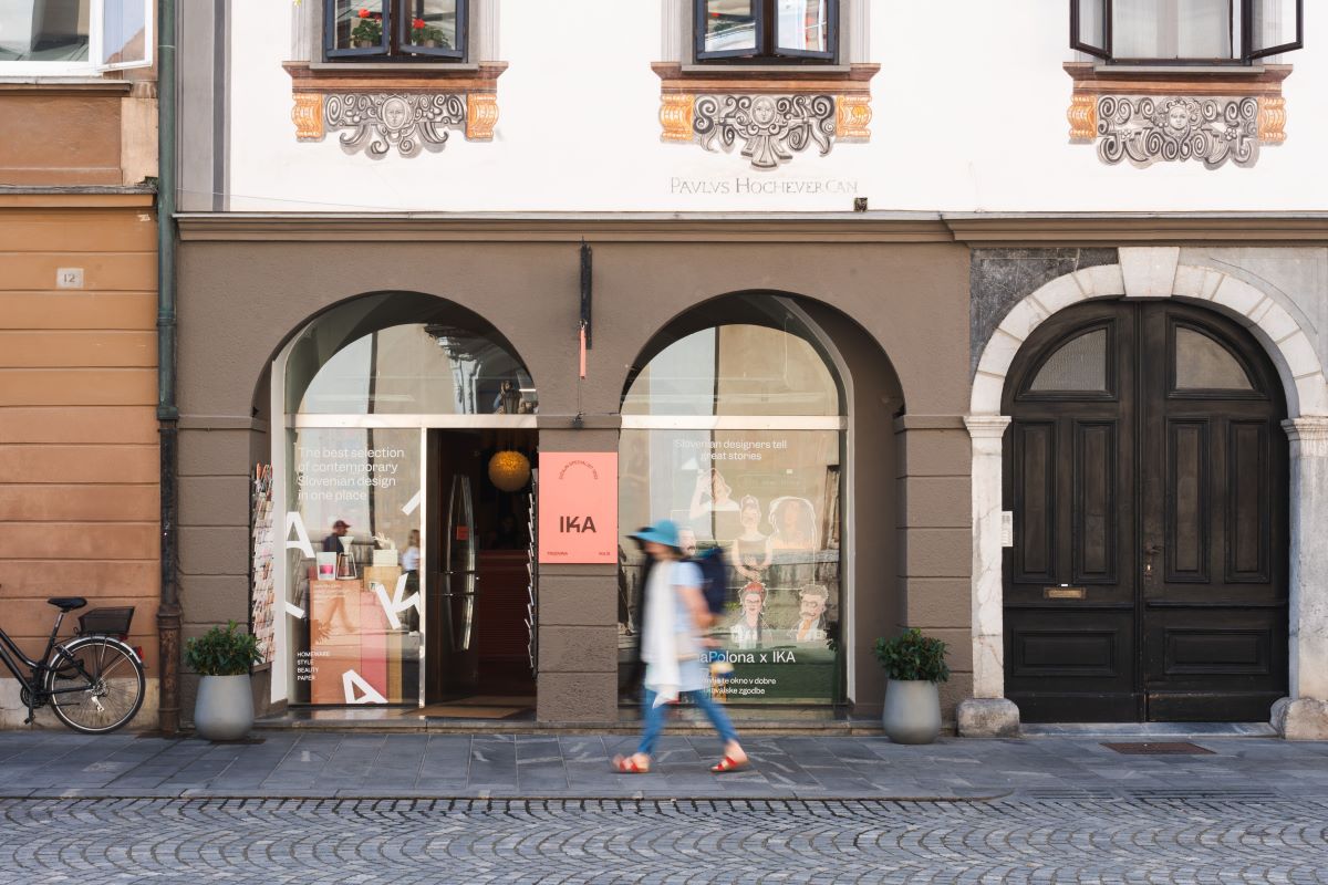 A woman walking past the white building with brown arches.