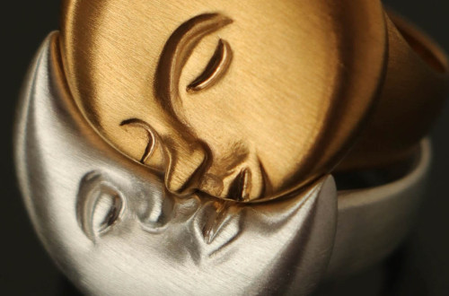 Gold and silver rings with sculpted faces of the sun and moon touching.