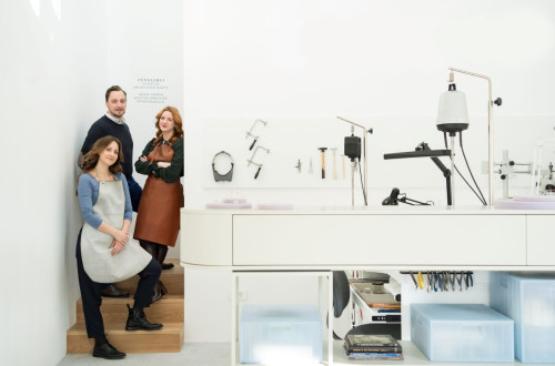 Ein modernes Juwelierstudio mit drei Handwerkern, die neben einem mit Werkzeugen und Maschinen ausgestatteten Arbeitsplatz posieren.