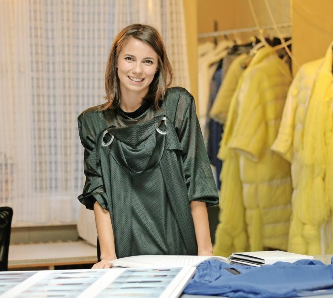 A smiling fashion designer in her workspace, surrounded by fabric samples and yellow fur coats.