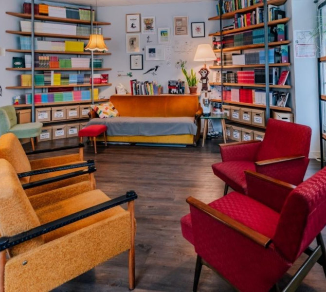 A cozy reading room with colorful armchairs, wooden bookshelves filled with books, and warm lighting.