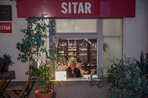 Ein gemütliches Geschäft namens "Sitar," von außen betrachtet, mit Menschen, die die warme Atmosphäre genießen.