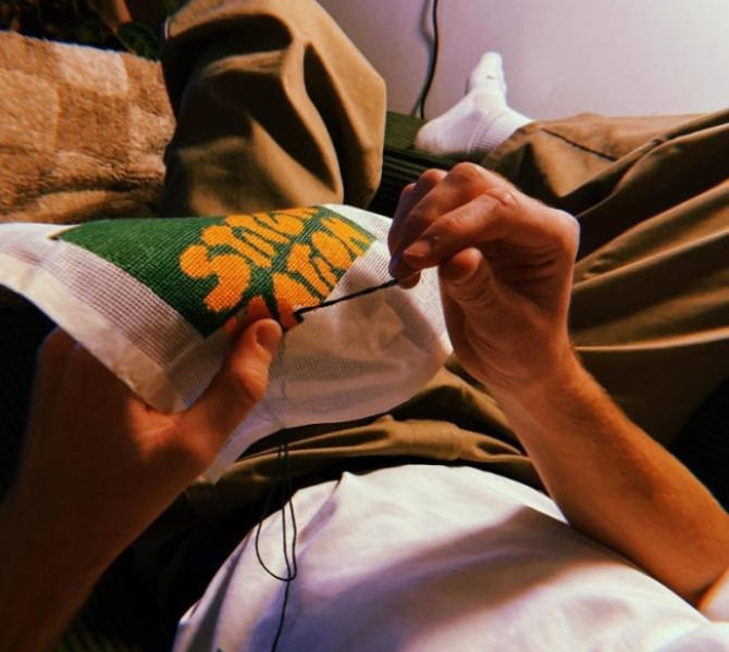 A person relaxing on a couch, carefully embroidering a colorful design on fabric.