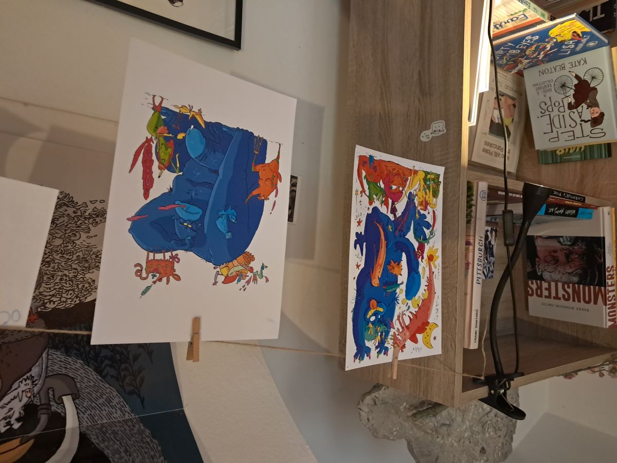 Colorful illustrations hanging on a string, displayed in a creative workspace with books and art materials.