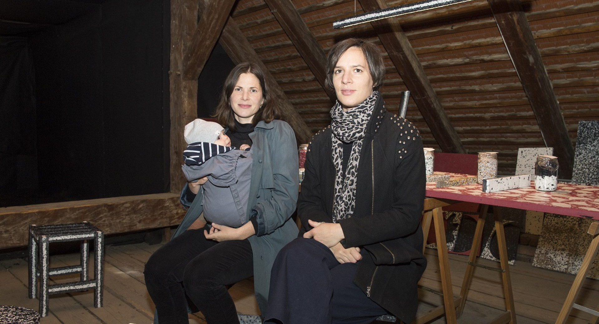 Two women are sitting on a bench. A woman is holding a child.