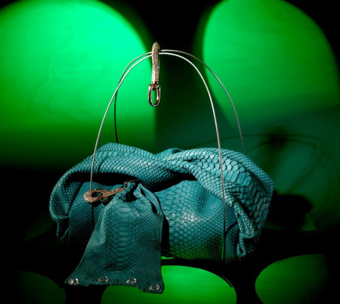 A striking turquoise handbag with a snakeskin texture, displayed under green lighting.
