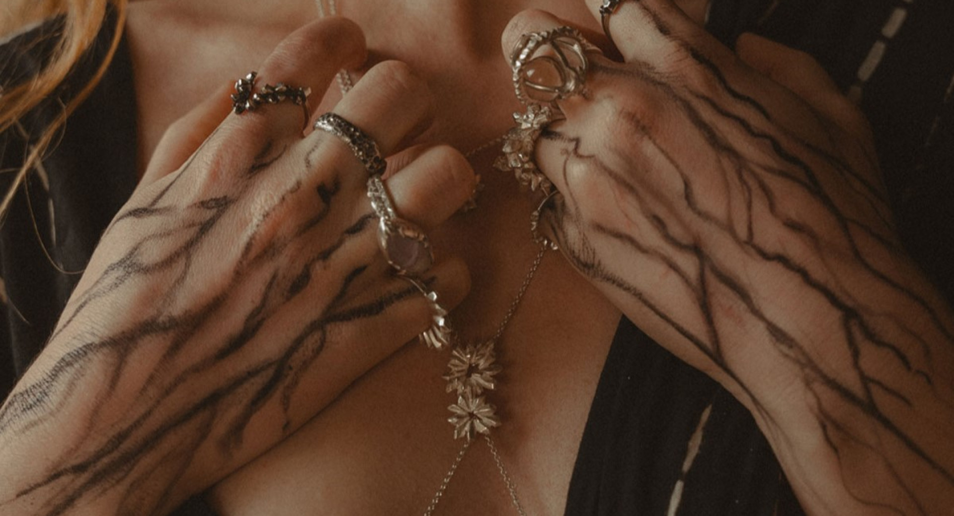 Un gros plan sur des mains ornées de bijoux en métal artistique, avec des bagues et un collier délicat.