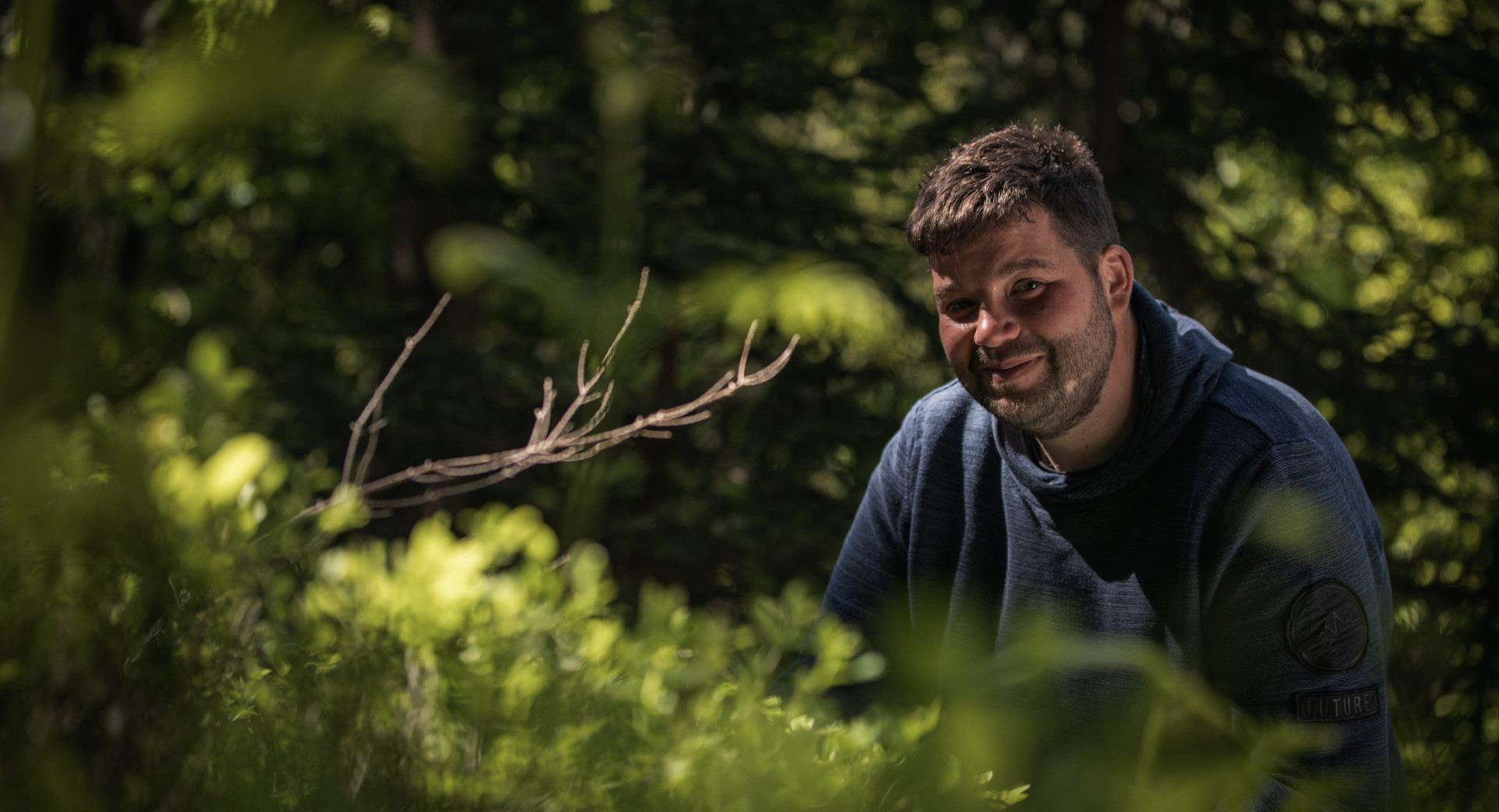 Moski v temno modrem puloverju cepi med zelenjem.