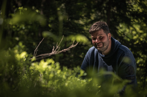 Moski v temno modrem puloverju cepi med zelenjem.