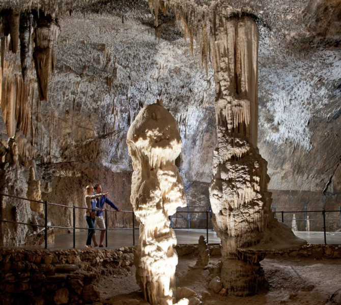 Una coppia in una grotta ammira due grandi concrezioni (stalattiti/stalagmiti).
