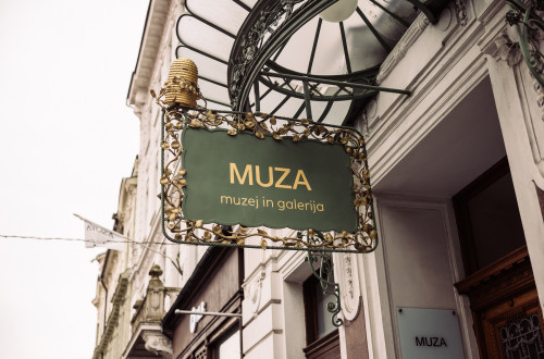 The exterior of the building with a dark green sign displaying the words "MUZA – museum and gallery" in Slovenian.