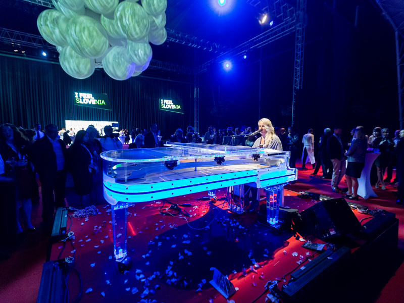 Glasbenica na klavirju. V ozadju gostje plešejo.