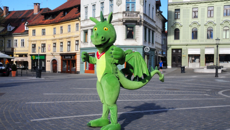 Big green dragon mascot on a city square. Houses in the background.