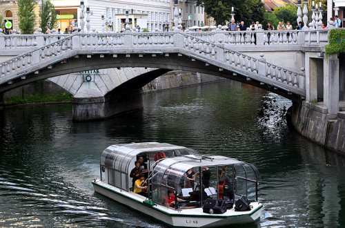 Turistična ladjica z obiskovalci. V ozadju Tromostovje.