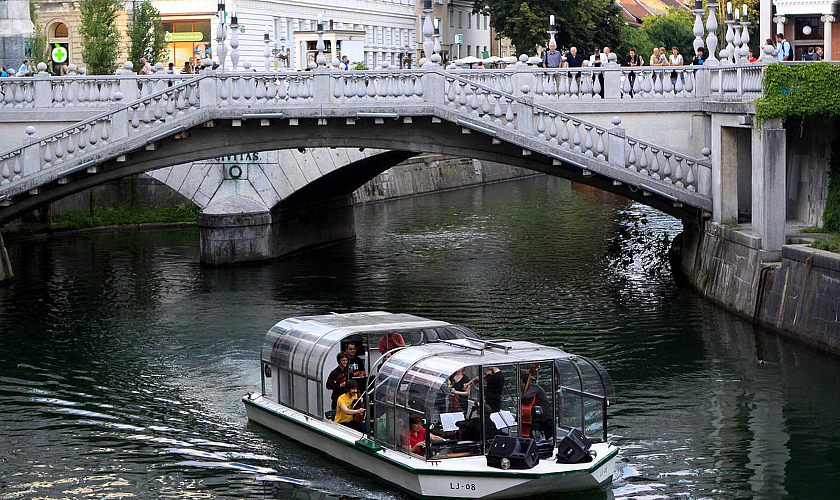 Turistična ladjica z obiskovalci. V ozadju Tromostovje.