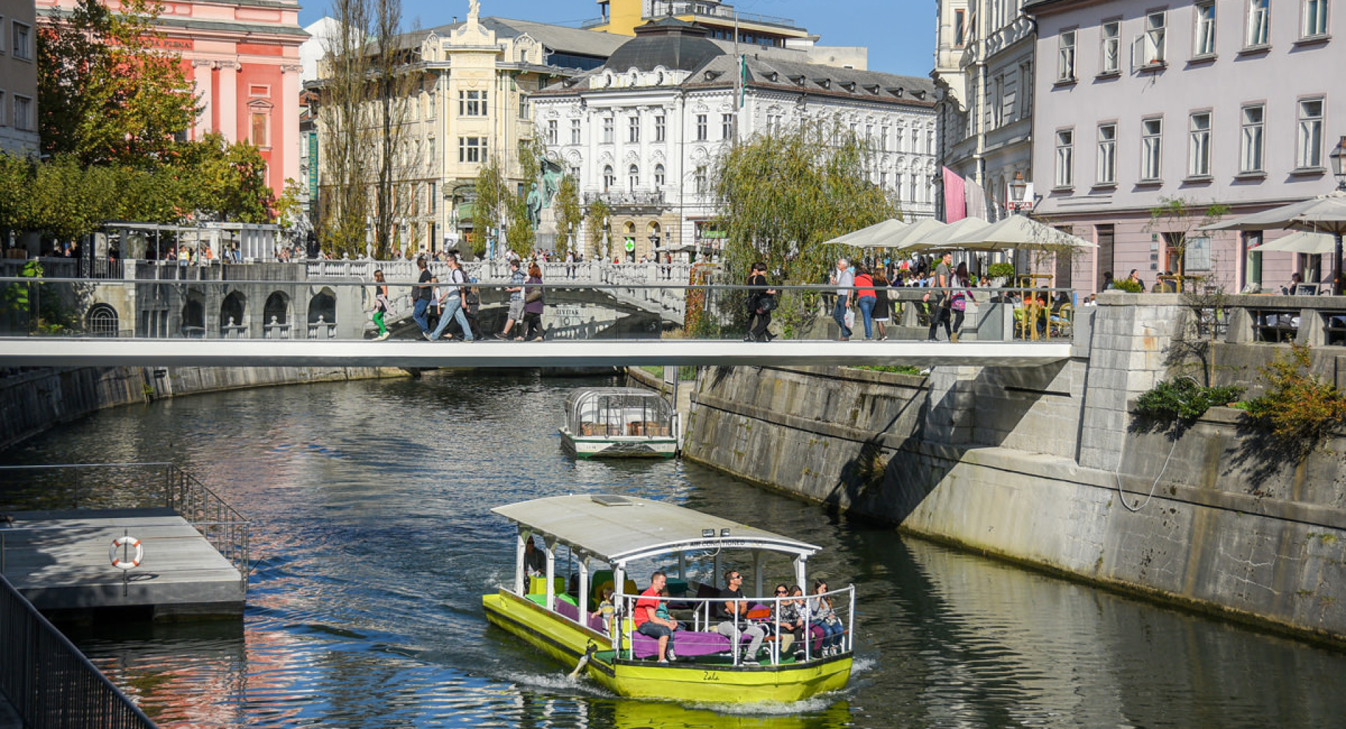 Turistična ladjica na Ljubljanici. V ozadju most in Tromostovje.