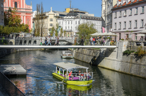 Turistična ladjica na Ljubljanici. V ozadju most in Tromostovje.