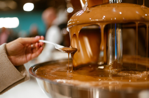 Zenska prislanja zlico k cokoladni fontani.