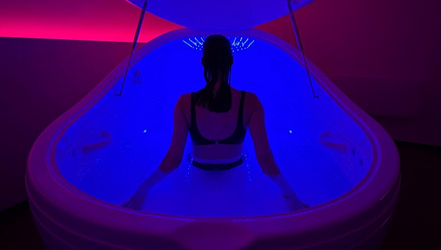 Person sitting in a float tank illuminated by soft ambient lighting.