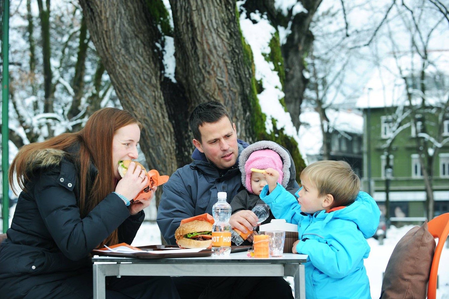 Družina ob mizi uživa v hamburgerjih.