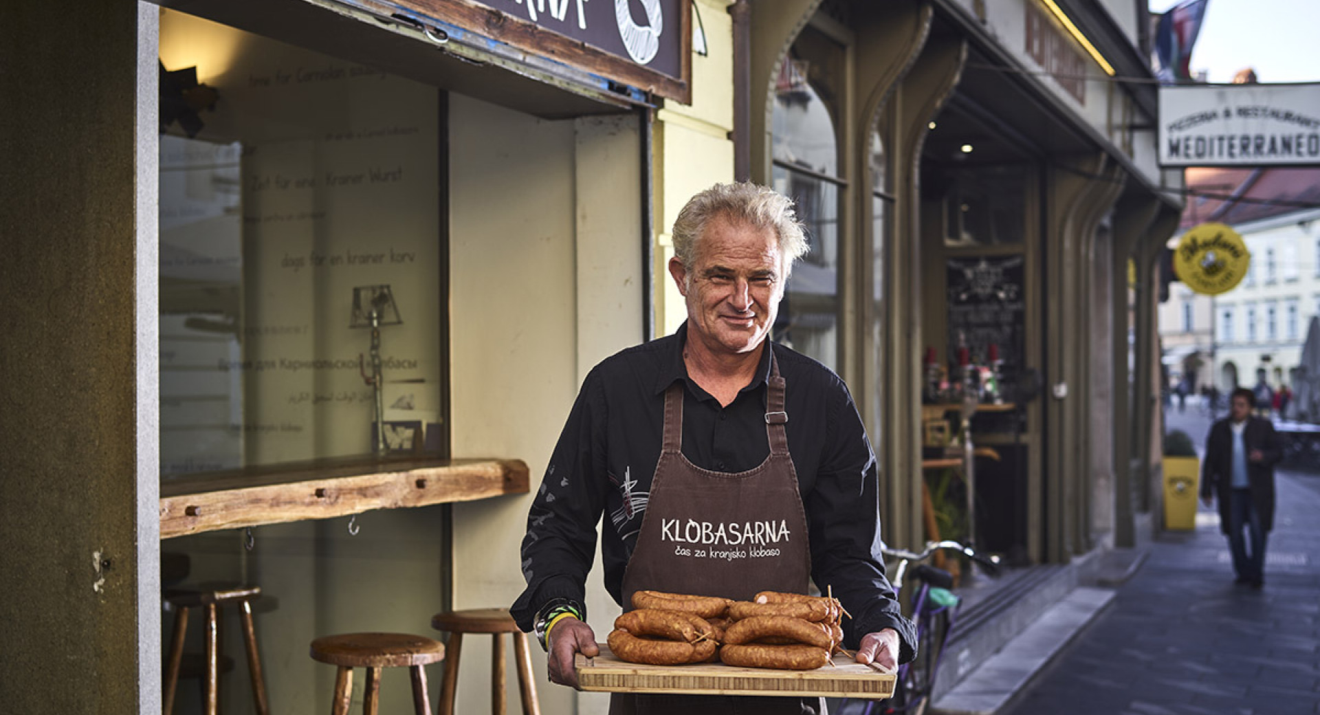 Gospod s klobasami na pladnju pred Klobasarno.