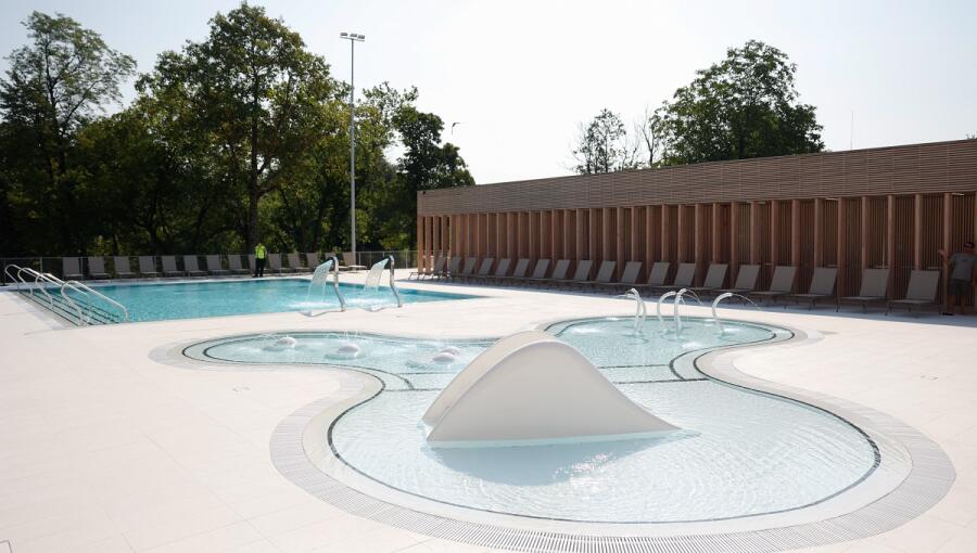 A large outdoor splash pool with sun loungers in the background.