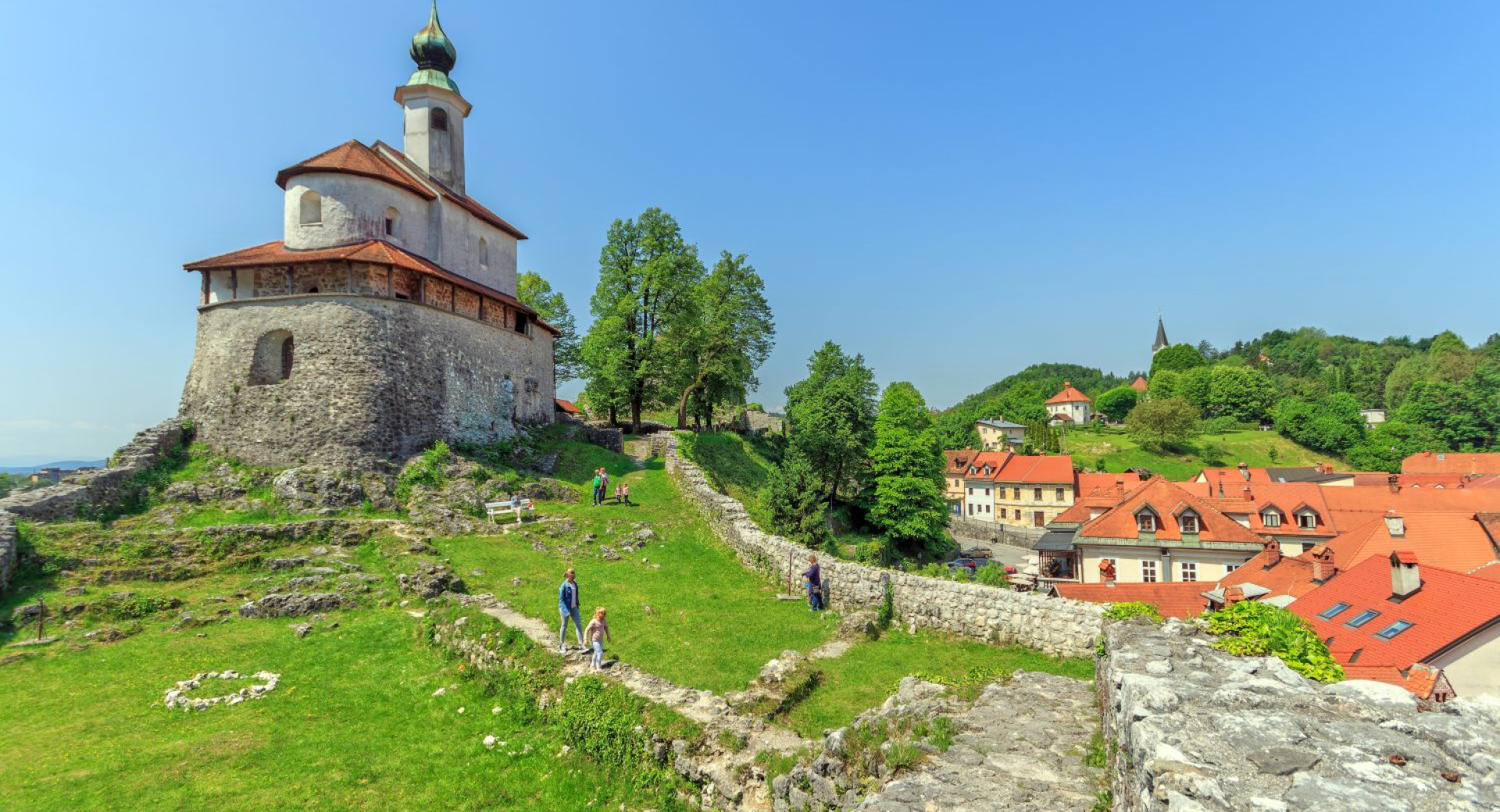 Cerkev na vzpetini nad srednjeveškim mestom. Okoli cerkve so vidni ostanki obzidja. 