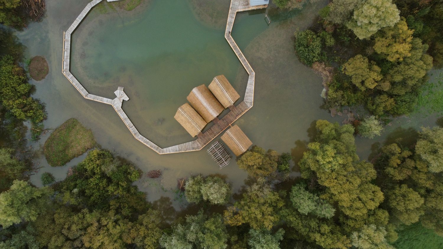 Thatched-roof houses from a bird's-eye view. Wooden houses next to a wooden platform and a pond.