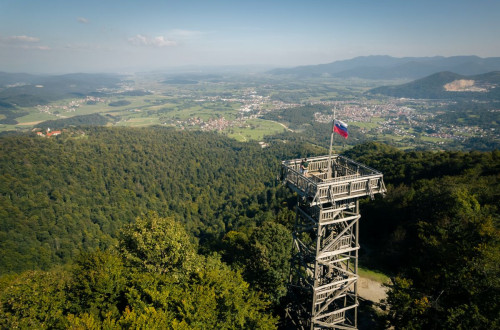 An observation tower with a flag. In the background, forest, meadows, and settlements.