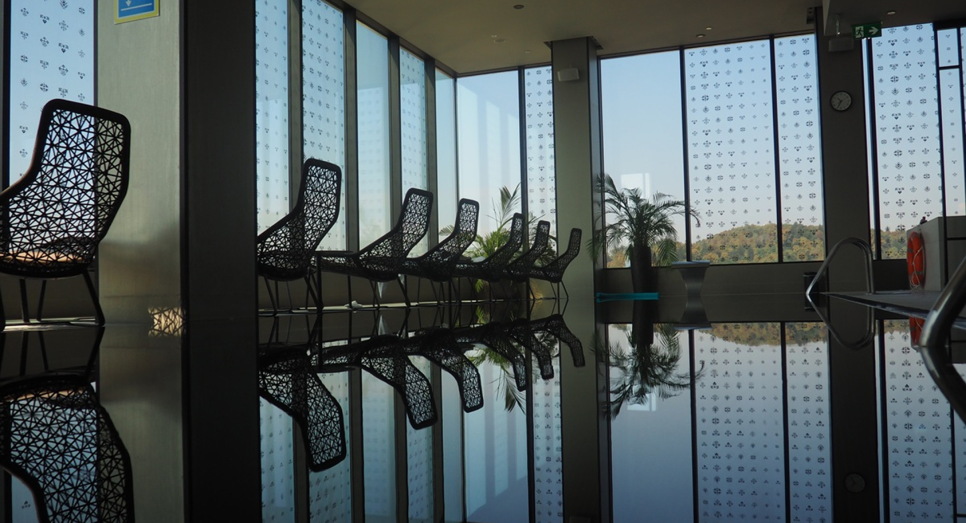 Panoramska okna od tal do stropa poleg bazena z lezalniki v ospredju.